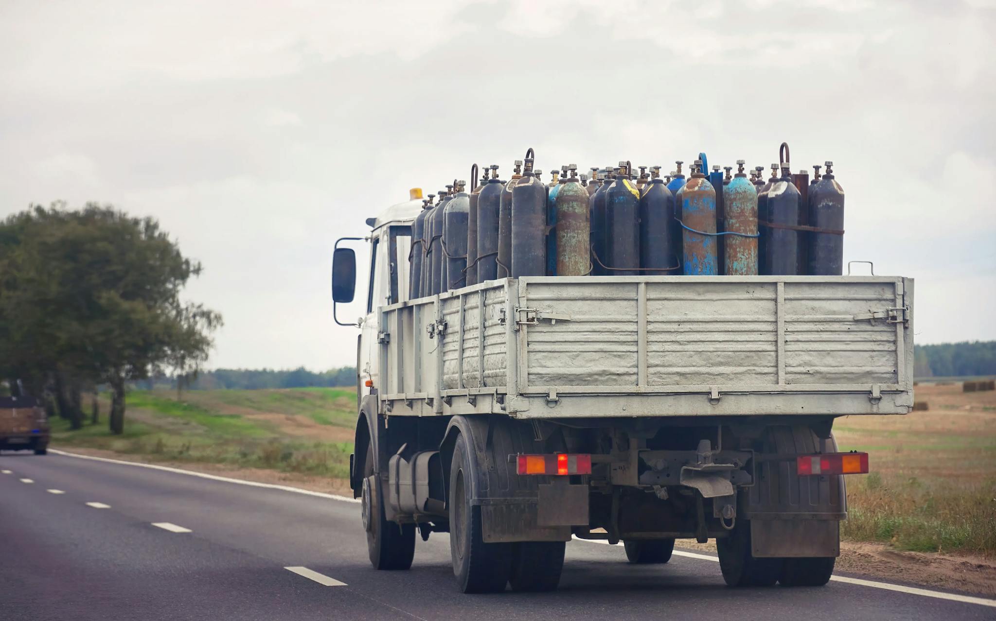 A truck transporting numerous oxygen cylinders on a country road.