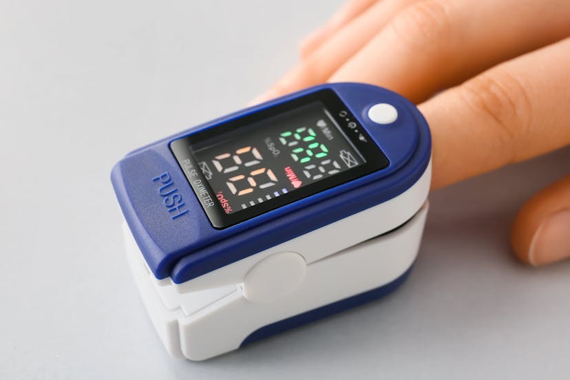 Close-up of a finger inserted into a blue and white digital pulse oximeter.