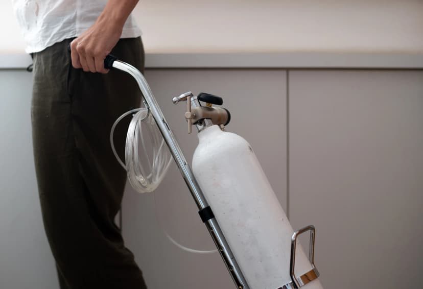 A person holding a portable oxygen cylinder with tubing and regulator.